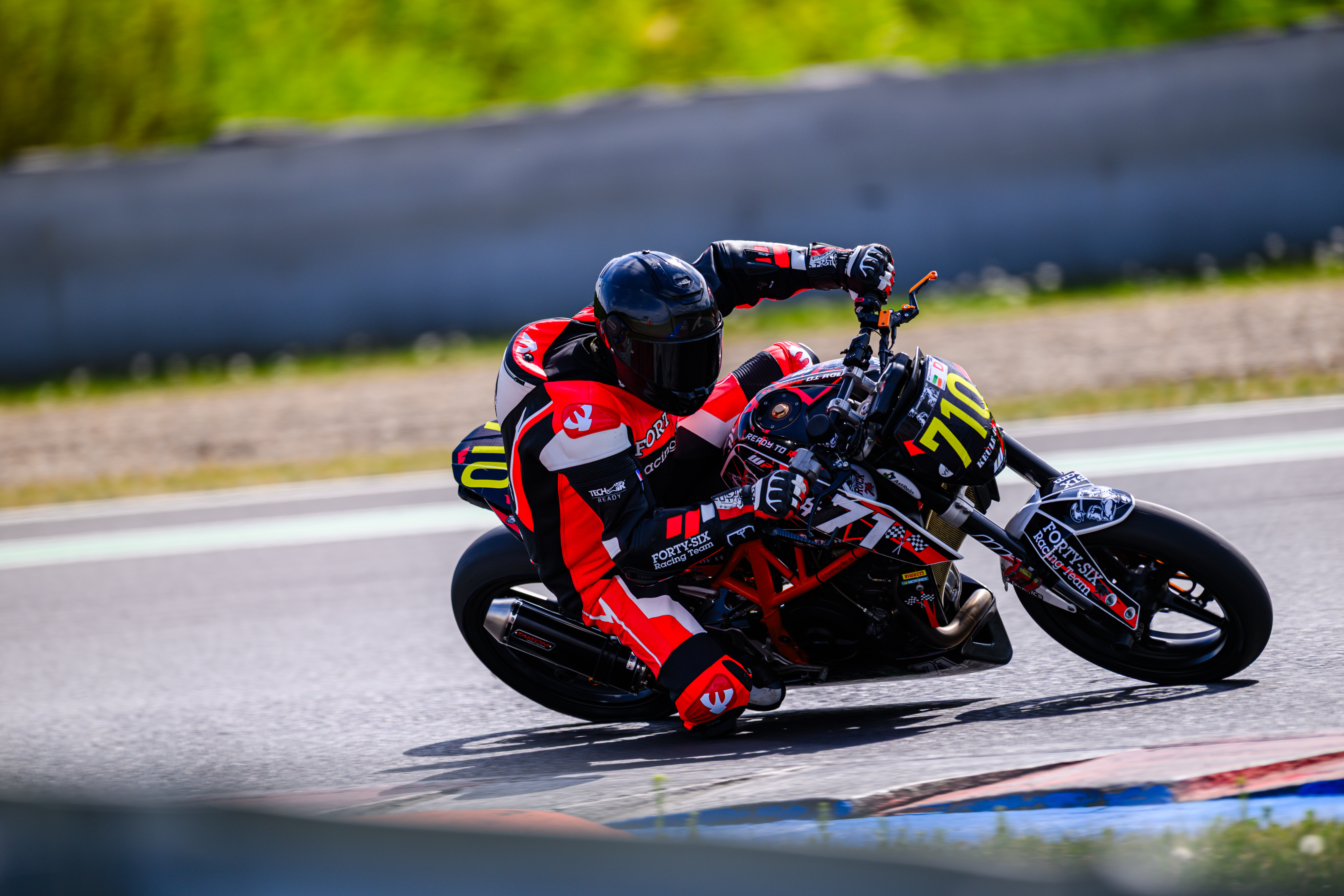 A motorcycle rider, clad in a red and black racing suit, leans into a turn on a race track, with the number 718 prominentl...